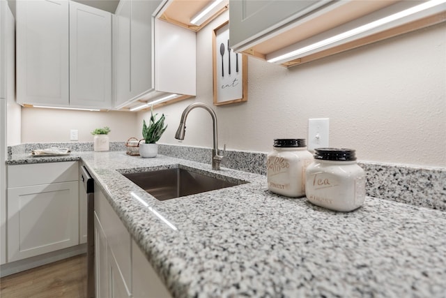 kitchen featuring white cabinetry, sink, stainless steel dishwasher, and light stone counters