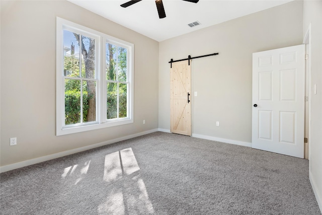 carpeted empty room featuring a barn door and ceiling fan