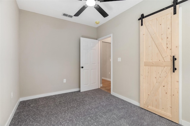 unfurnished bedroom featuring ceiling fan, a barn door, and carpet