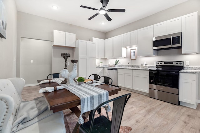 kitchen with light stone countertops, appliances with stainless steel finishes, white cabinetry, sink, and light wood-type flooring