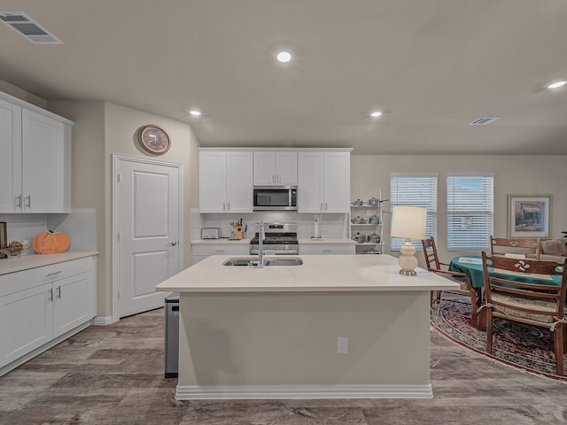 kitchen featuring appliances with stainless steel finishes, sink, light hardwood / wood-style floors, white cabinets, and a kitchen island with sink