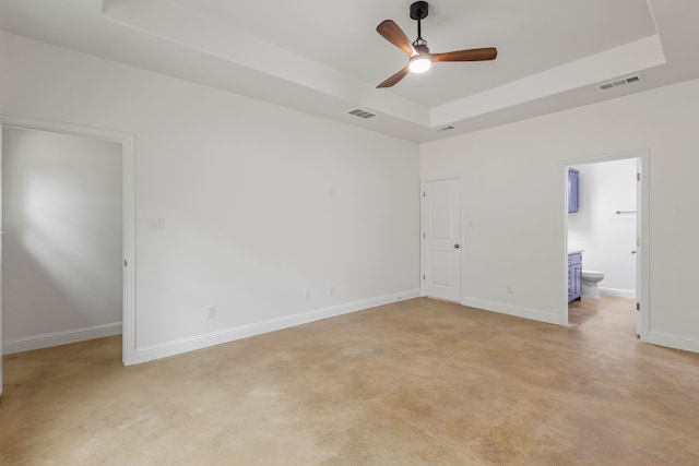 unfurnished bedroom with a tray ceiling, ceiling fan, and ensuite bathroom