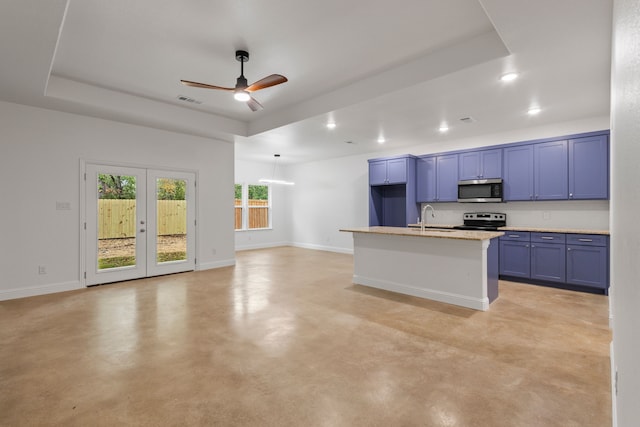 kitchen with an island with sink, appliances with stainless steel finishes, sink, and a tray ceiling