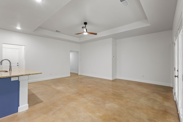 unfurnished living room with ceiling fan, a raised ceiling, sink, and light colored carpet