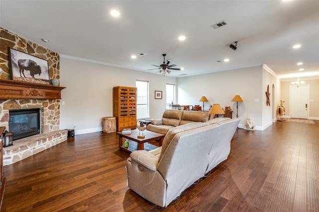 living room with a stone fireplace, ceiling fan with notable chandelier, dark hardwood / wood-style floors, and crown molding