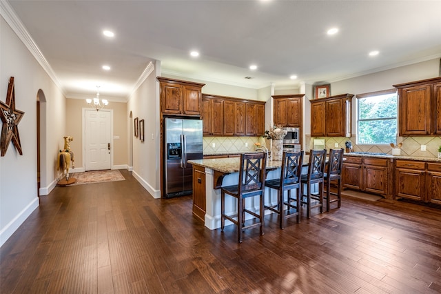 kitchen featuring a breakfast bar, appliances with stainless steel finishes, a kitchen island with sink, crown molding, and dark hardwood / wood-style flooring