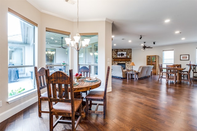 dining area with a stone fireplace, ceiling fan with notable chandelier, a healthy amount of sunlight, and dark hardwood / wood-style floors