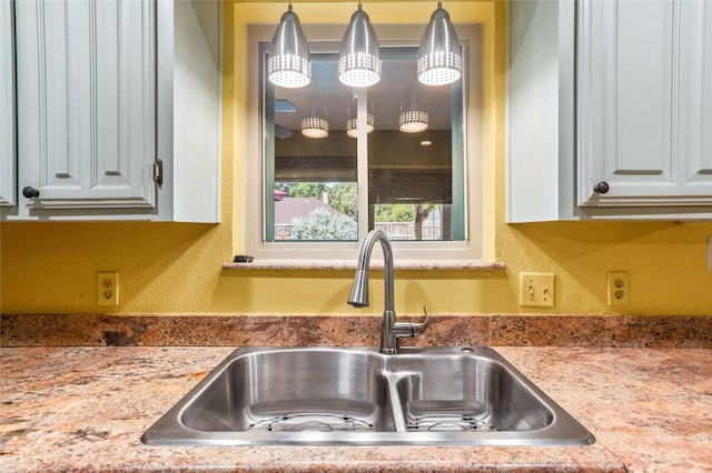 kitchen with decorative light fixtures, sink, and white cabinets