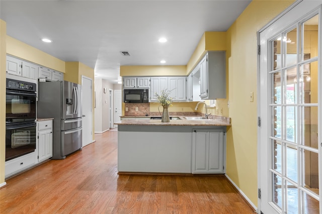 kitchen featuring sink, light hardwood / wood-style flooring, backsplash, black appliances, and kitchen peninsula