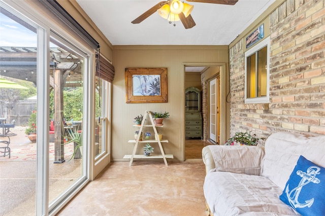 living area featuring ceiling fan and brick wall