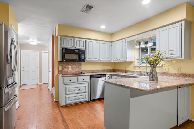 kitchen with appliances with stainless steel finishes, light stone countertops, sink, kitchen peninsula, and light hardwood / wood-style flooring