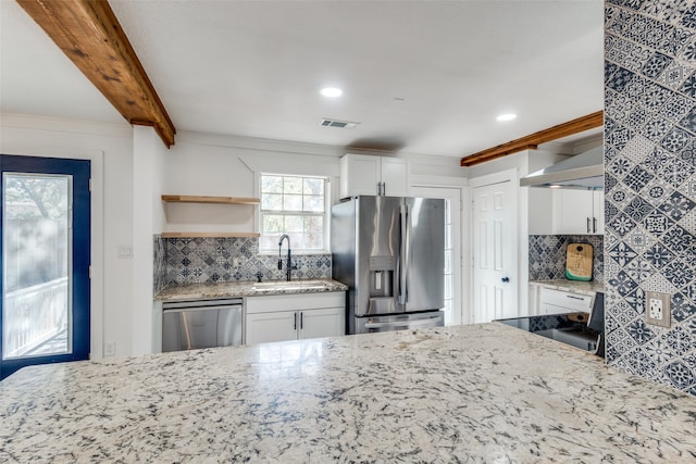 kitchen with beam ceiling, white cabinets, light stone counters, and stainless steel appliances