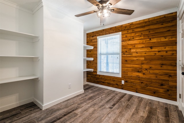 empty room with dark hardwood / wood-style flooring, wooden walls, crown molding, and ceiling fan