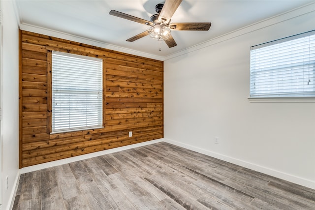 empty room featuring ceiling fan, wooden walls, wood-type flooring, and ornamental molding