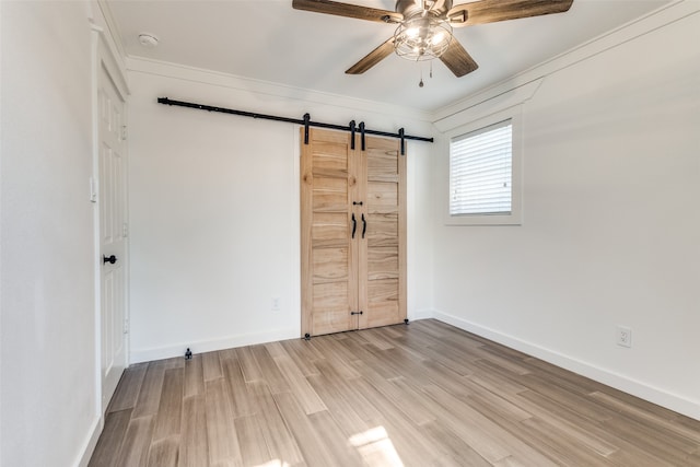 unfurnished bedroom featuring ceiling fan, light hardwood / wood-style flooring, crown molding, a barn door, and a closet