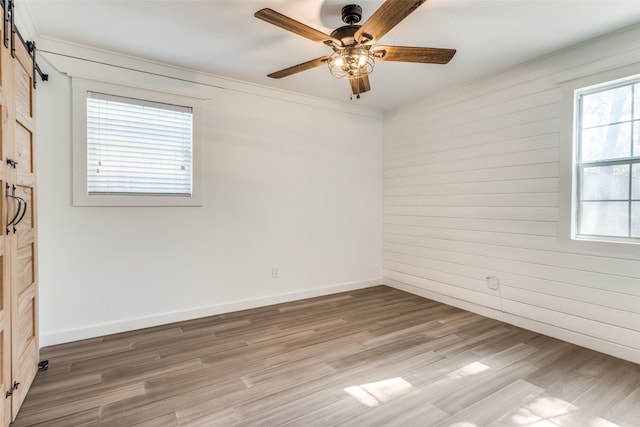 empty room with a barn door, wood-type flooring, and ceiling fan