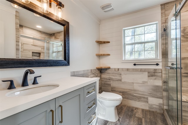 bathroom with hardwood / wood-style floors, vanity, an enclosed shower, toilet, and tile walls