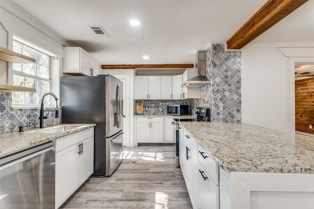 kitchen with white cabinets, tasteful backsplash, wall chimney range hood, light stone countertops, and appliances with stainless steel finishes