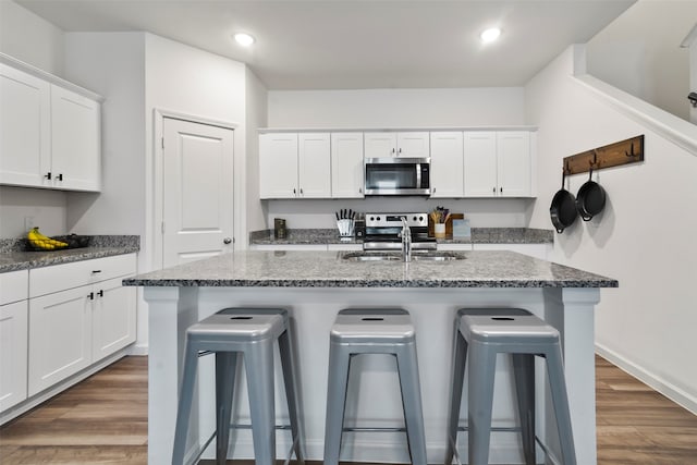 kitchen with stainless steel appliances, a breakfast bar area, a center island with sink, and dark hardwood / wood-style floors