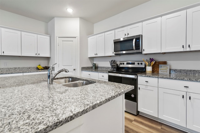 kitchen featuring stainless steel appliances, light hardwood / wood-style floors, light stone counters, sink, and white cabinetry