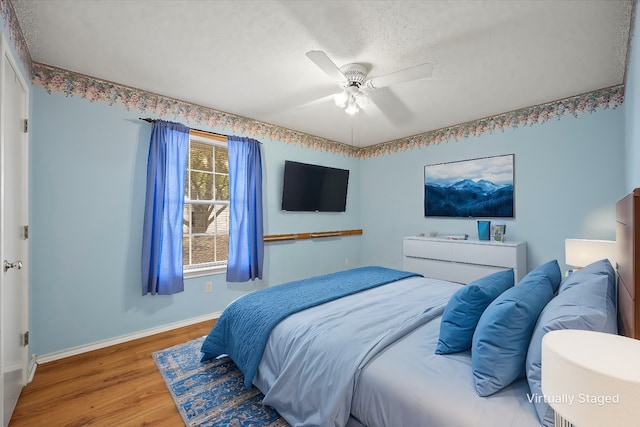 bedroom with ceiling fan, wood-type flooring, and a textured ceiling