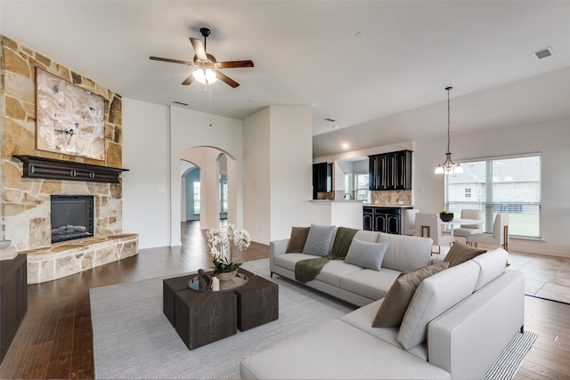 living room featuring a stone fireplace, wood-type flooring, and ceiling fan with notable chandelier