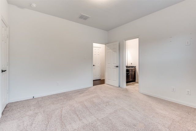 unfurnished bedroom with ensuite bathroom and light carpet