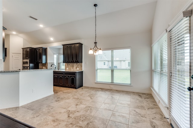 kitchen with stainless steel microwave, pendant lighting, lofted ceiling, light stone counters, and dark brown cabinets