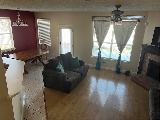 living room with a fireplace, ceiling fan, a textured ceiling, and light wood-type flooring