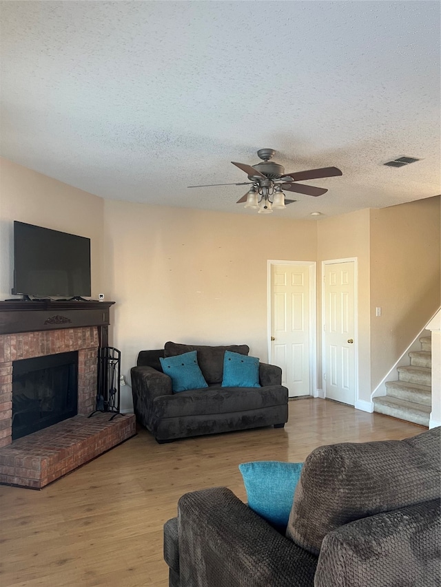 living room with a brick fireplace, wood-type flooring, a textured ceiling, and ceiling fan