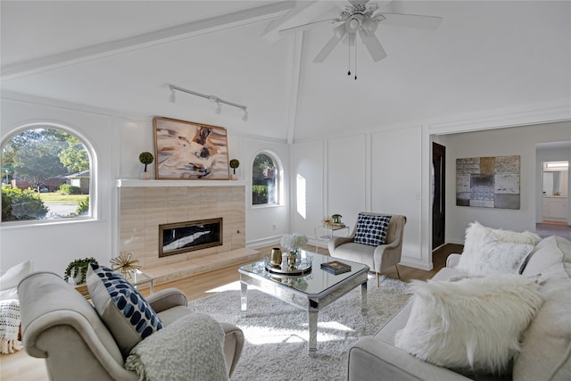 living room with beamed ceiling, light hardwood / wood-style floors, a healthy amount of sunlight, and a tiled fireplace