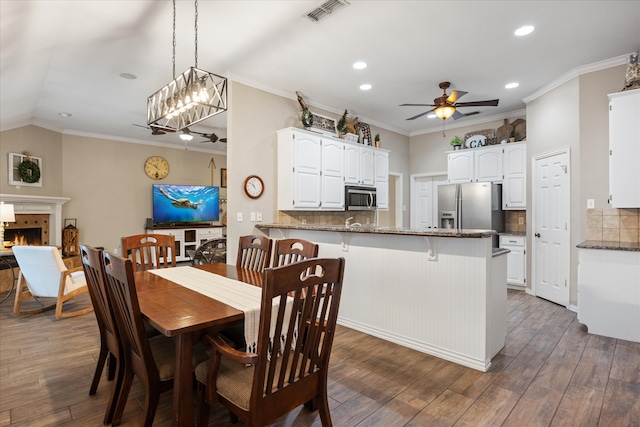 dining area with dark hardwood / wood-style flooring, a tile fireplace, ornamental molding, and ceiling fan with notable chandelier