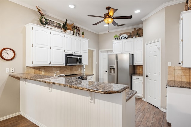 kitchen with wood-type flooring, stainless steel appliances, dark stone counters, white cabinets, and kitchen peninsula