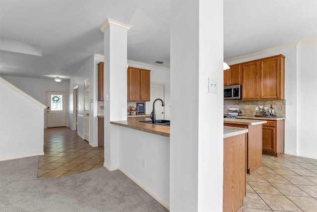 kitchen with backsplash, sink, light tile patterned flooring, kitchen peninsula, and decorative columns