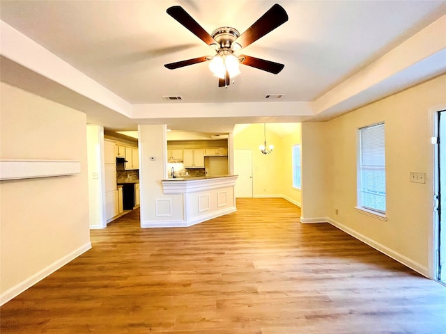 unfurnished living room with ceiling fan with notable chandelier, light hardwood / wood-style floors, and a raised ceiling