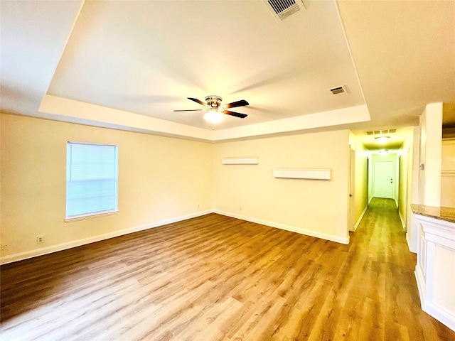 spare room featuring ceiling fan, light wood-type flooring, and a tray ceiling