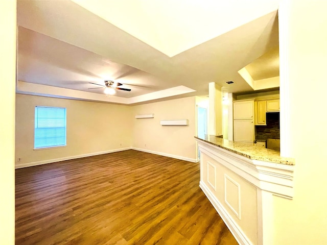 unfurnished living room featuring a tray ceiling, ceiling fan, and dark wood-type flooring