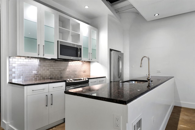 kitchen with stainless steel appliances, sink, dark stone countertops, white cabinets, and decorative backsplash