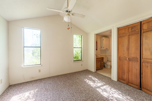 unfurnished bedroom featuring multiple windows, vaulted ceiling, light colored carpet, and a textured ceiling