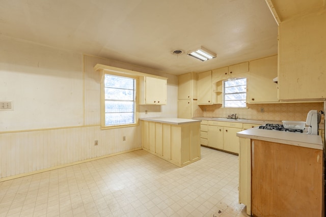 kitchen featuring sink, backsplash, kitchen peninsula, cream cabinetry, and wood walls