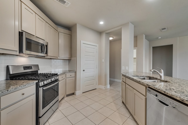 kitchen with tasteful backsplash, stainless steel appliances, light tile patterned floors, light stone countertops, and sink