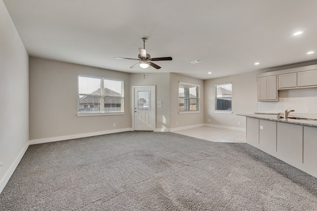 unfurnished living room featuring ceiling fan, light carpet, and sink