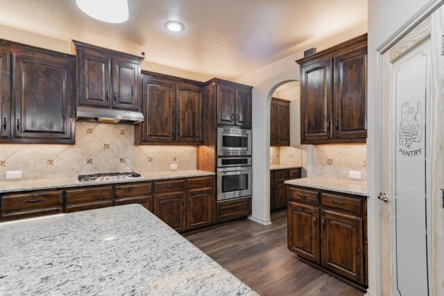 2216 Rosalinda Pass, Fort Worth, TX 76131 - kitchen featuring appliances with stainless steel finishes, under cabinet range hood, arched walkways, dark wood finished floors, and light stone counters