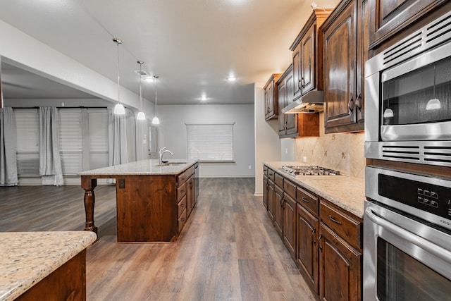 kitchen with a center island with sink, stainless steel appliances, dark hardwood / wood-style floors, hanging light fixtures, and a breakfast bar area