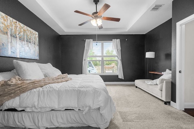 carpeted bedroom featuring a tray ceiling and ceiling fan