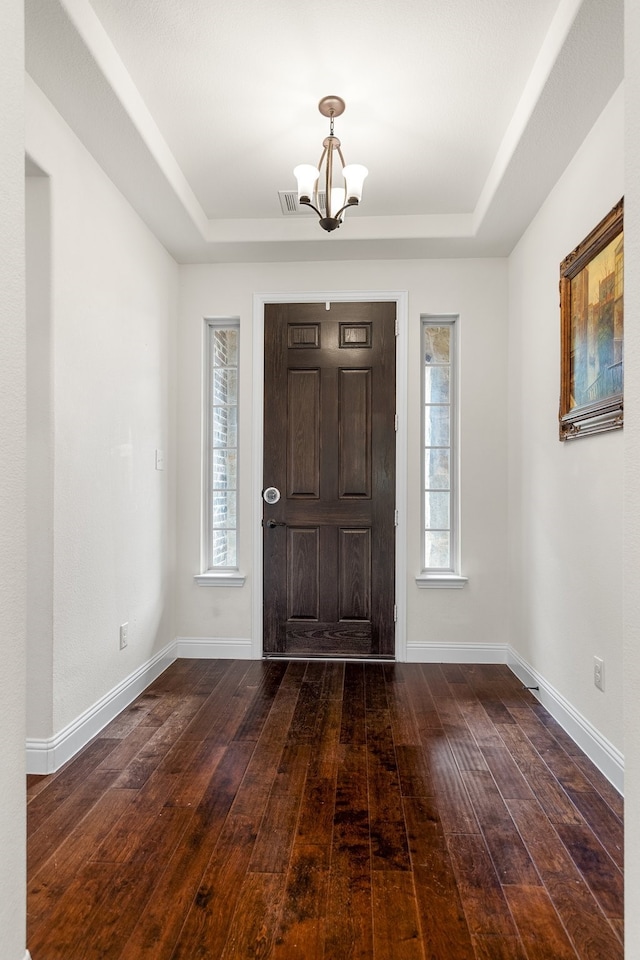 foyer entrance featuring dark hardwood / wood-style flooring, a chandelier, and a raised ceiling