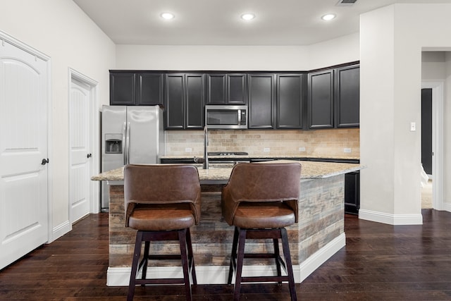 kitchen featuring a kitchen island with sink, light stone counters, and appliances with stainless steel finishes