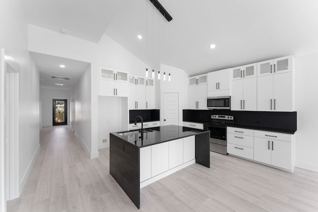 kitchen featuring appliances with stainless steel finishes, white cabinetry, high vaulted ceiling, an island with sink, and decorative light fixtures