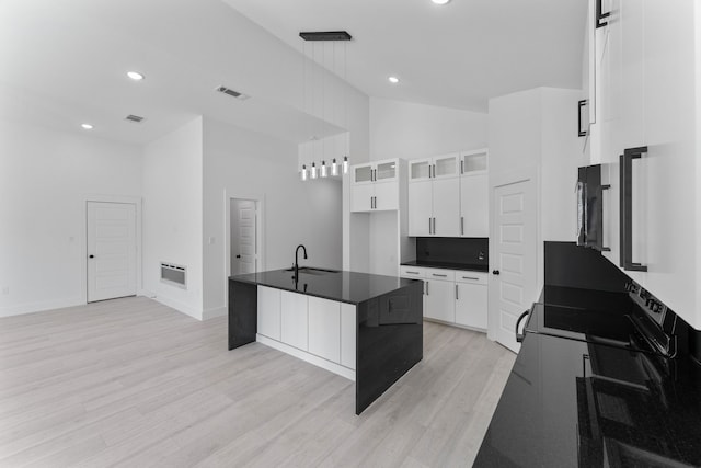 kitchen featuring sink, white cabinetry, an island with sink, a towering ceiling, and light hardwood / wood-style floors