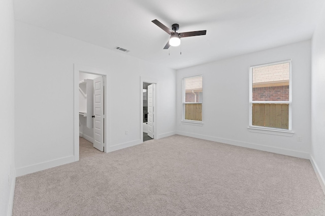 unfurnished bedroom with ceiling fan, connected bathroom, a spacious closet, and light colored carpet